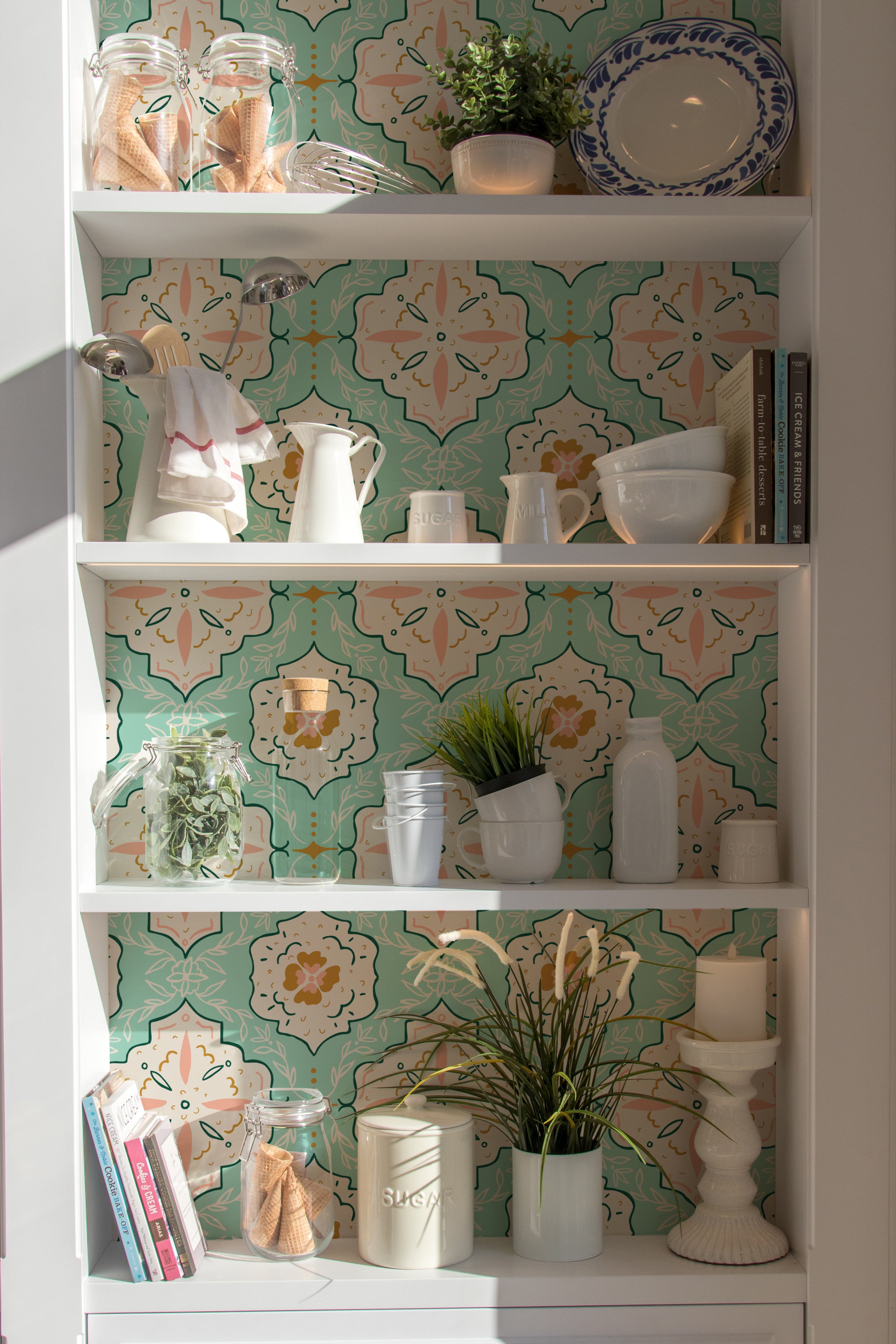 "Interior shelving unit decorated with Fatima Tile Wallpaper featuring intricate Moroccan-style patterns in turquoise, peach, and white, displaying kitchen items like pots and cookbooks.