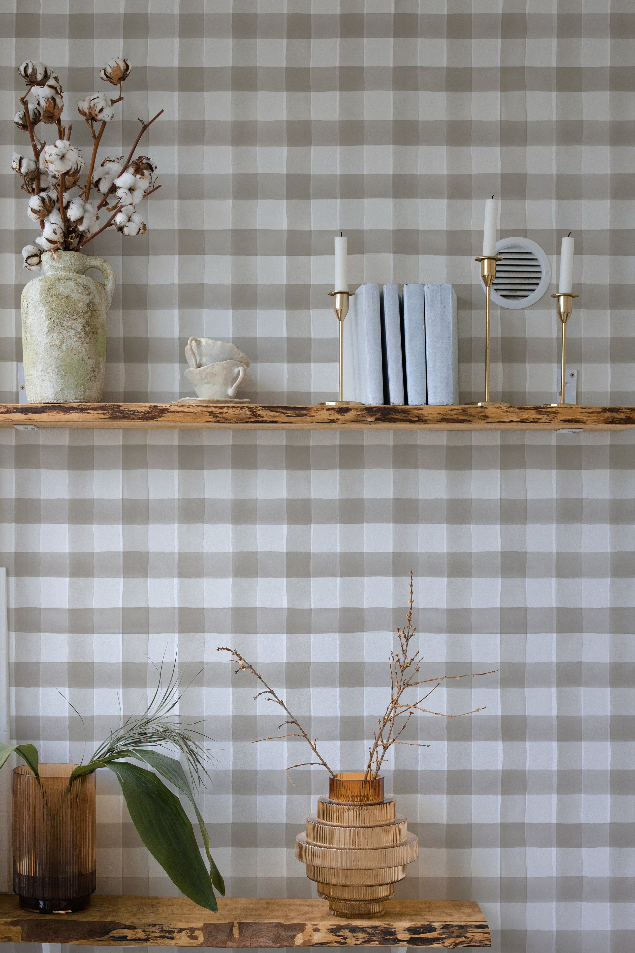 An alternate decor setup using the same Cuadro de Búfalo wallpaper, now in a stylish grey and white buffalo check pattern. The scene is accented with rustic decor elements like a wooden shelf holding a vase with dried branches and candle holders.