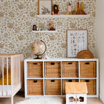 A cozy nursery room wall covered in vintage sparrow wallpaper with golden bird and leaf motifs. The room includes a baby crib, white storage unit with wicker baskets, a small globe, and floating shelves holding toys and books.