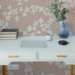A modern workspace featuring a white desk with minimalist design elements, enhanced by the charming Fleur de Printemps Wallpaper showcasing large, simple white floral patterns on a soft pink background.