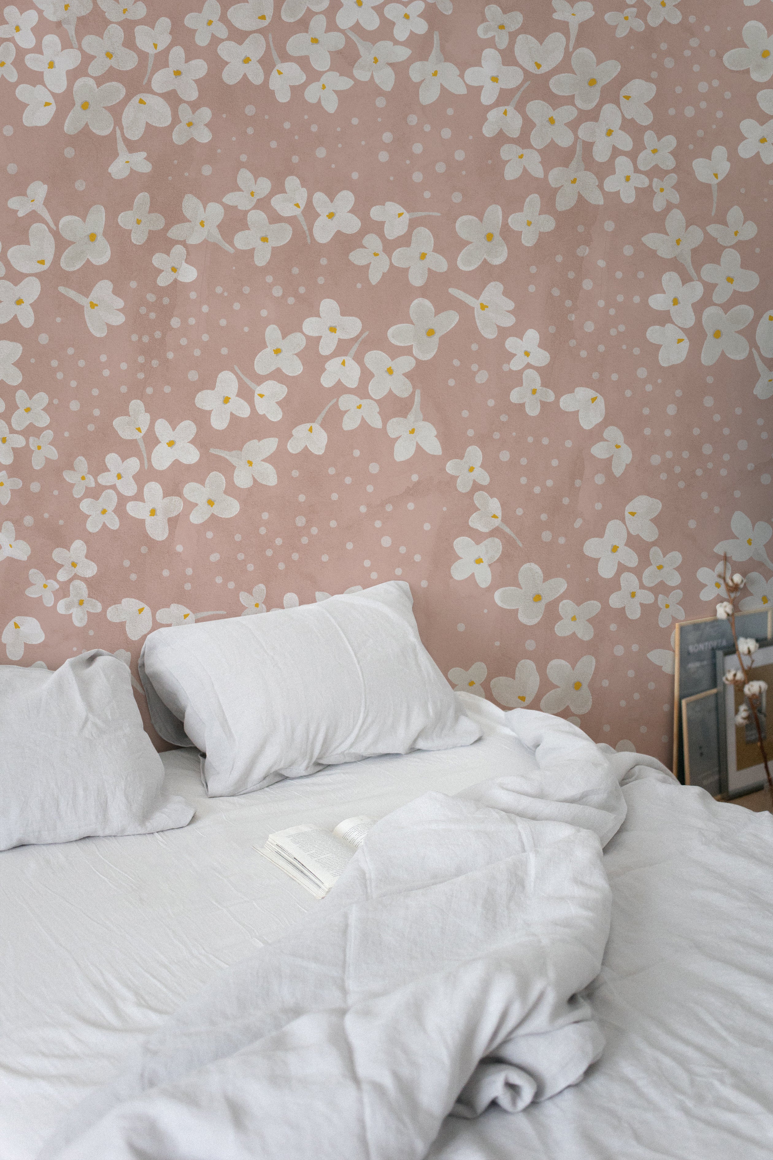 A cozy bedroom setup where the Fleur de Printemps Wallpaper provides a calm and soothing backdrop with its white flowers and subtle polka dots over a pastel pink background.