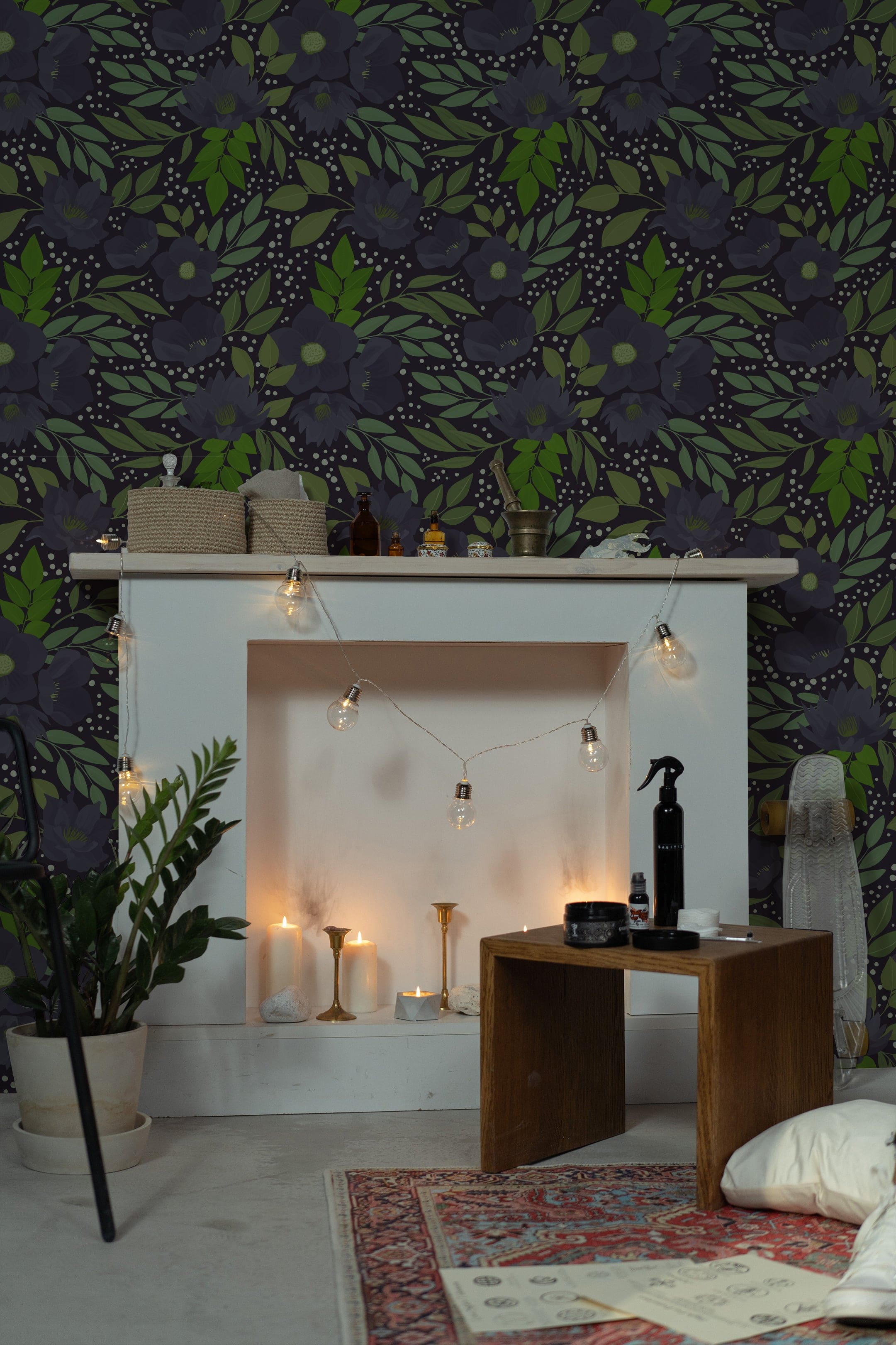 A cozy, warmly lit living area featuring the Martinique Floral Wallpaper, characterized by its large-scale dark purple flowers and lush green leaves on a dark background. The wallpaper creates a bold statement while providing a backdrop to a serene space decorated with candles and string lights.