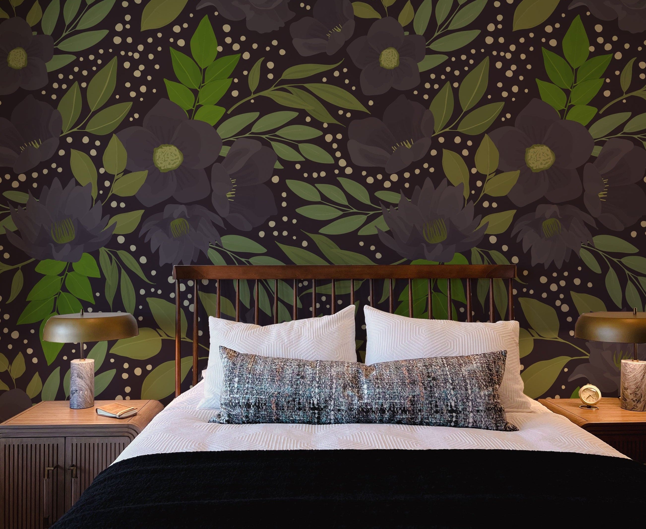 Modern bedroom with a striking floral wallpaper featuring large dark flowers and green foliage on a dark background, a wooden bed with white bedding and a black blanket, white and patterned pillows, wooden nightstands with green-shaded lamps, and small decorative items