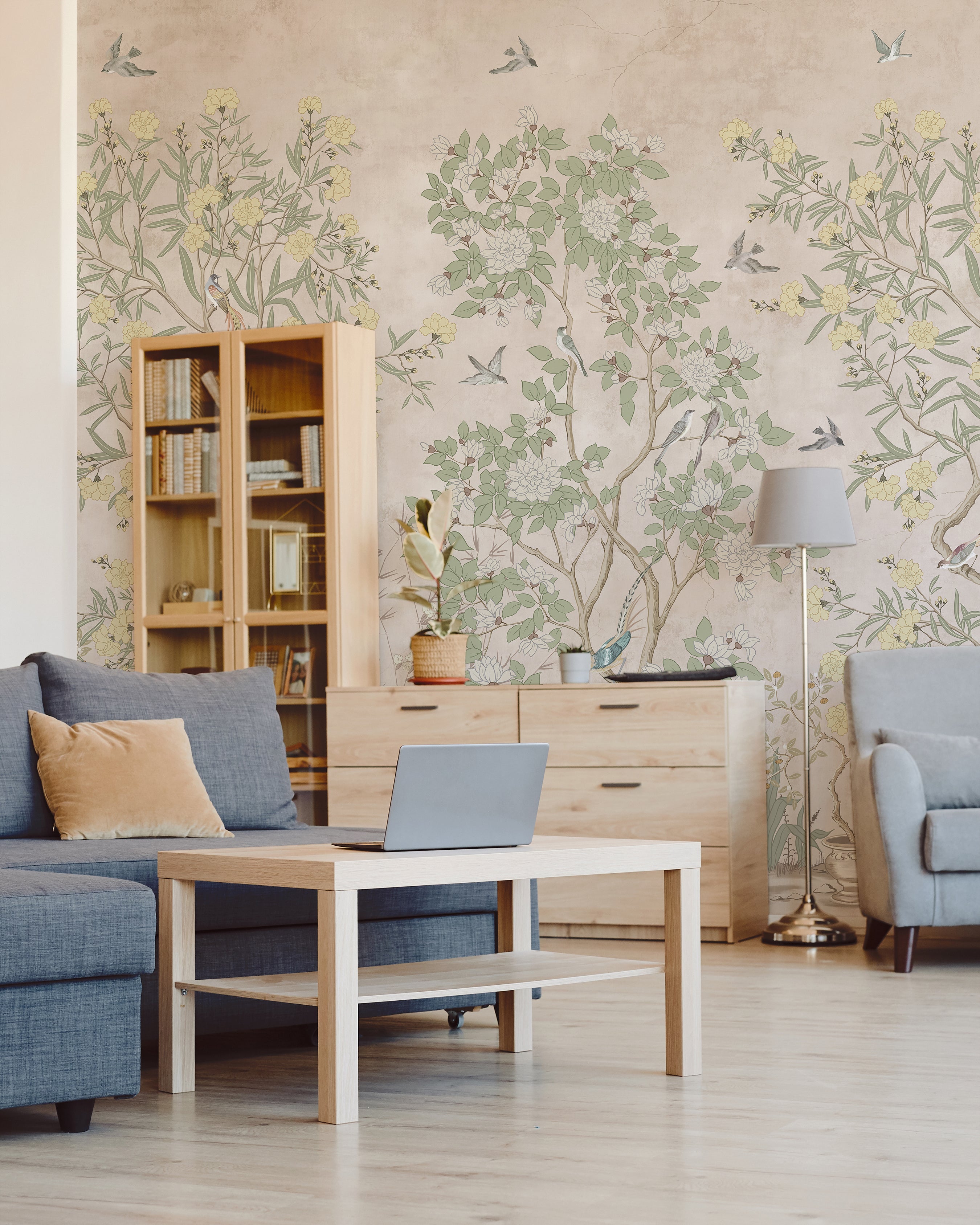Image of a cozy home office area with chinoiserie wallpaper featuring a delicate tree and bird design that adds a peaceful and artistic backdrop to the room furnished with a light wood desk, shelving, and blue textiles