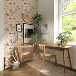 Home office setup with a desk and chair against a wall adorned with peach and green floral wallpaper, complemented by indoor plants