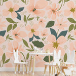 Children's play area with small white chairs and toys in front of a wall covered in soft peach floral wallpaper