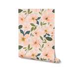 A mockup of rolled wallpaper with a pattern of peach and green floral design on a light pink background.