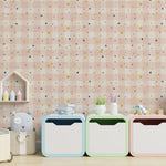 A close-up view of a nursery room wall with pastel pink wallpaper featuring a subtle grid and small, colorful triangles, complemented by modern children's storage furniture and decorative items