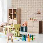 A children's playroom with walls covered in a cheerful pink wallpaper adorned with a colorful confetti-like pattern of triangles, paired with wooden furniture and bright toys