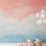 Wallpaper with a gradient from pastel pink to blue resembling a calm sky, installed on a wall, accompanied by decorative items including balloons, a star lamp, and a wicker basket."