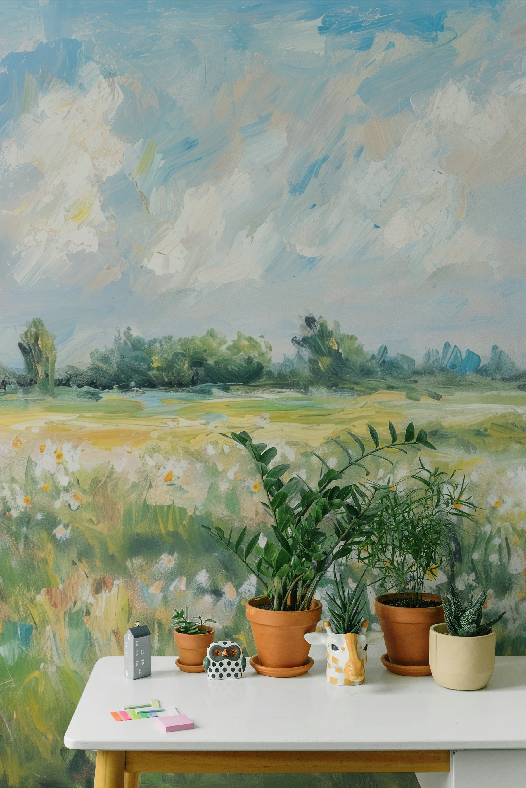 Close-up of the Impressionist mural wallpaper in a room decorated with potted plants, highlighting the delicate details of the meadow and the soft, pastel-colored sky.