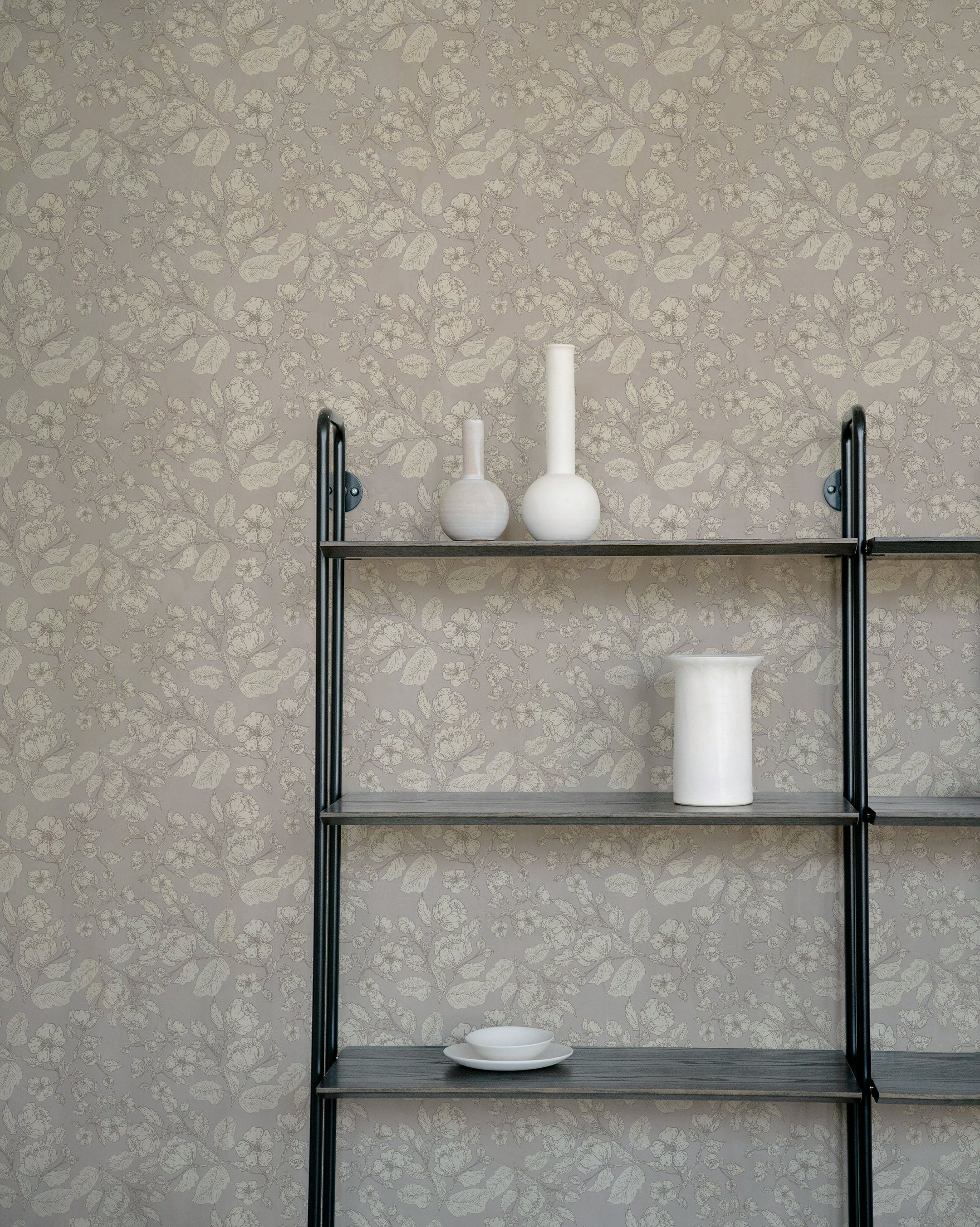 A minimalist shelf displaying white vases and dishes against the Château Wallpaper, featuring an intricate floral pattern in soft taupe. The wallpaper adds a touch of elegance and subtle sophistication to the background.