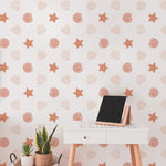 A chic home office setup with Mermaid Shells Wallpaper, creating a bright and inviting workspace. The wall features a pattern of delicate seashells and starfish, complemented by a modern white desk and green houseplants.