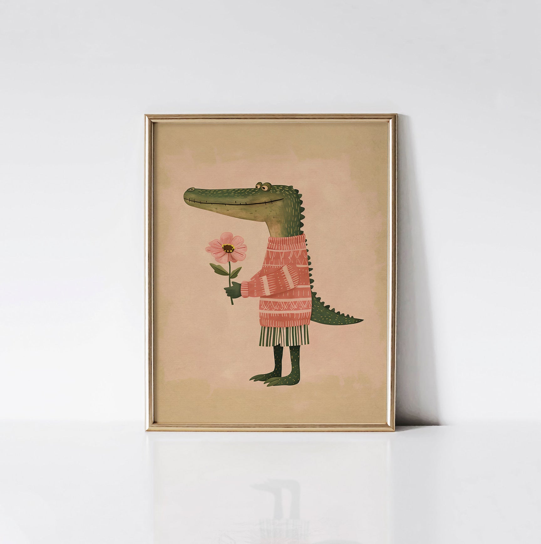 The 'Gentle Gator Blooms' art print displayed in a sleek gold frame, featuring a friendly alligator in a pink sweater holding a flower.