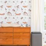 A nursery room showcasing the Woodland Wonder Wallpaper, with playful and gentle illustrations of woodland creatures that create a calm and nurturing environment. The room features minimalist furniture, enhancing the wallpaper's soothing tones.