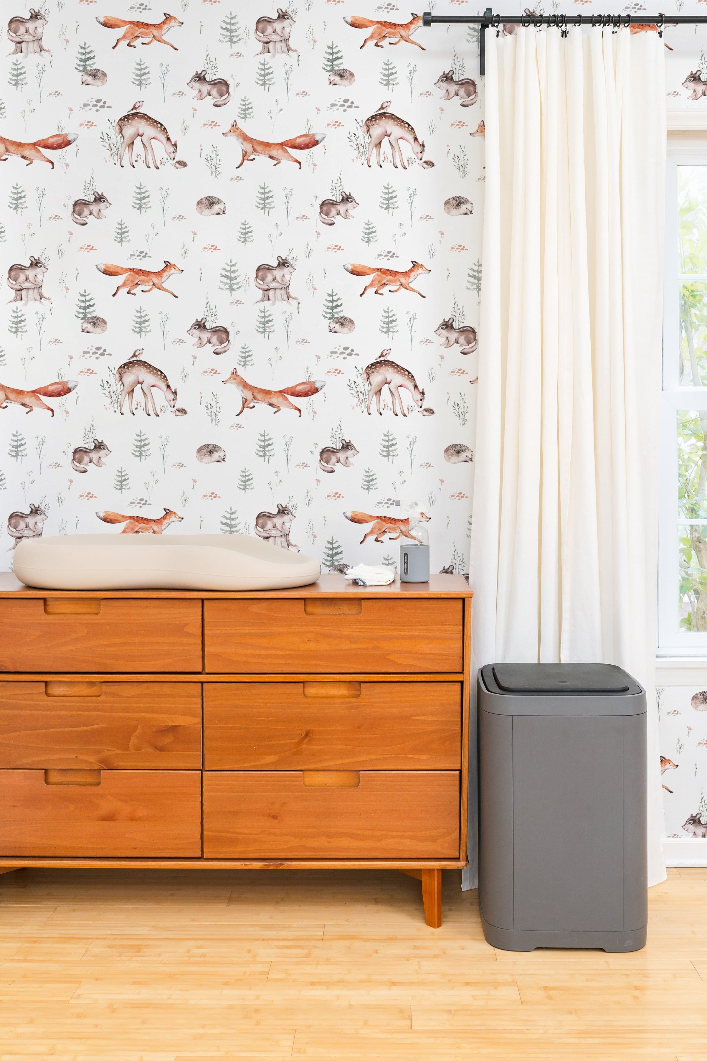 A nursery room showcasing the Woodland Wonder Wallpaper, with playful and gentle illustrations of woodland creatures that create a calm and nurturing environment. The room features minimalist furniture, enhancing the wallpaper's soothing tones.