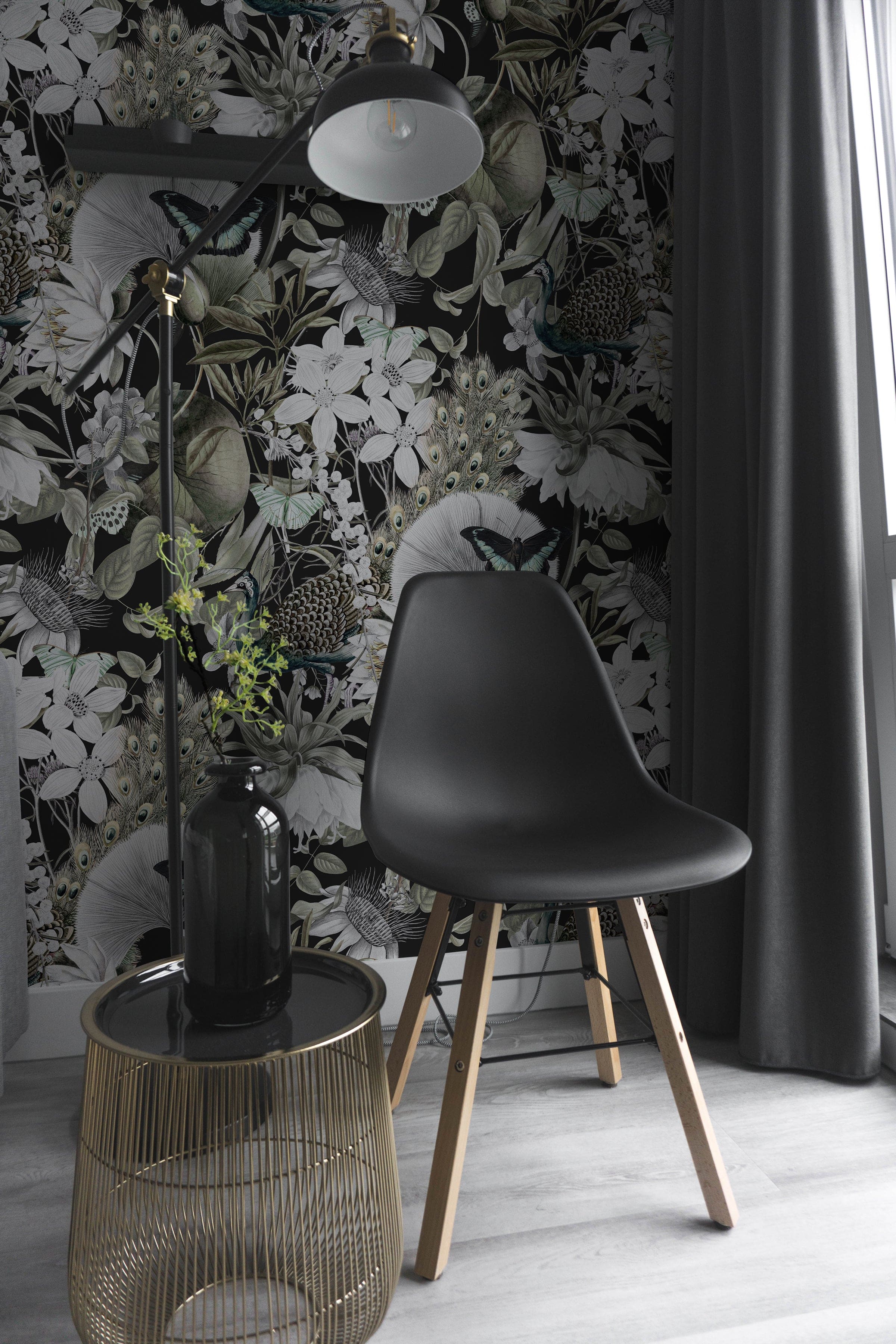 A sophisticated corner of a room featuring the 'Moody Botanicals Wallpaper' with lush botanical and peacock motifs in shades of black, grey, and white. A modern black chair and a stylish metal side table complement the dramatic and detailed design of the wallpaper, creating a chic and elegant space