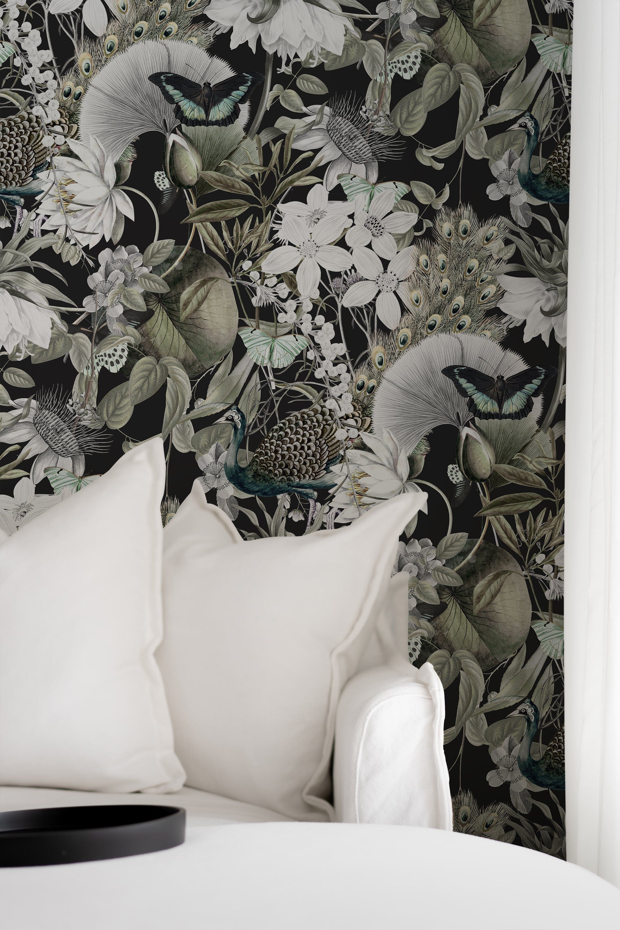A cozy nook enhanced by the 'Moody Botanicals Wallpaper', adding depth and intrigue to the space. The detailed black and white botanical and animal designs provide a striking backdrop to a simple white sofa adorned with neutral pillows, merging comfort with high style