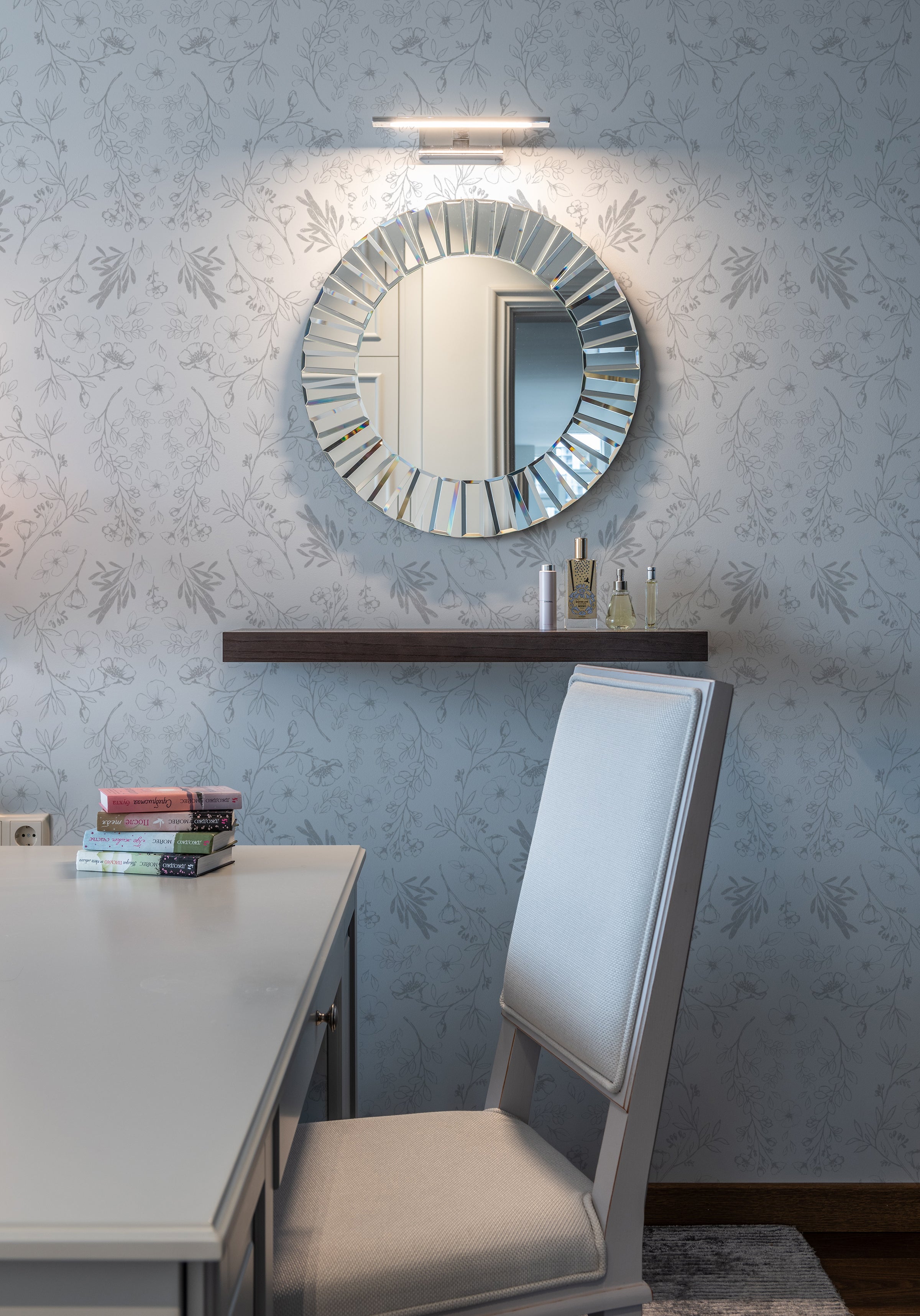 An intimate vanity corner with Rustic Vintage Floral wallpaper creating a delicate backdrop for a modern circular mirror and a dark wooden shelf, blending vintage charm with contemporary design