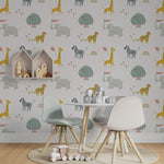 A children's playroom decorated with Safari Adventure Wallpaper showing elephants, giraffes, zebras, and cheetahs in soft colors. The room includes a small kids' table with chairs, a circular rug, and wooden toys enhancing the playful, adventurous theme.
