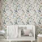 A cozy nursery room featuring a floral wallpaper with a design of large and small flowers in shades of beige, cream, blue, and green. The room includes a white crib with a soft gray blanket and a pillow, wooden blocks on the floor, and a round storage basket nearby.