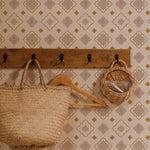 Wall-mounted wooden coat rack with hooks holding a woven tote bag and a small basket against a wall adorned with Moroccan Mosaic Wallpaper, featuring beige, blush, and gold geometric patterns