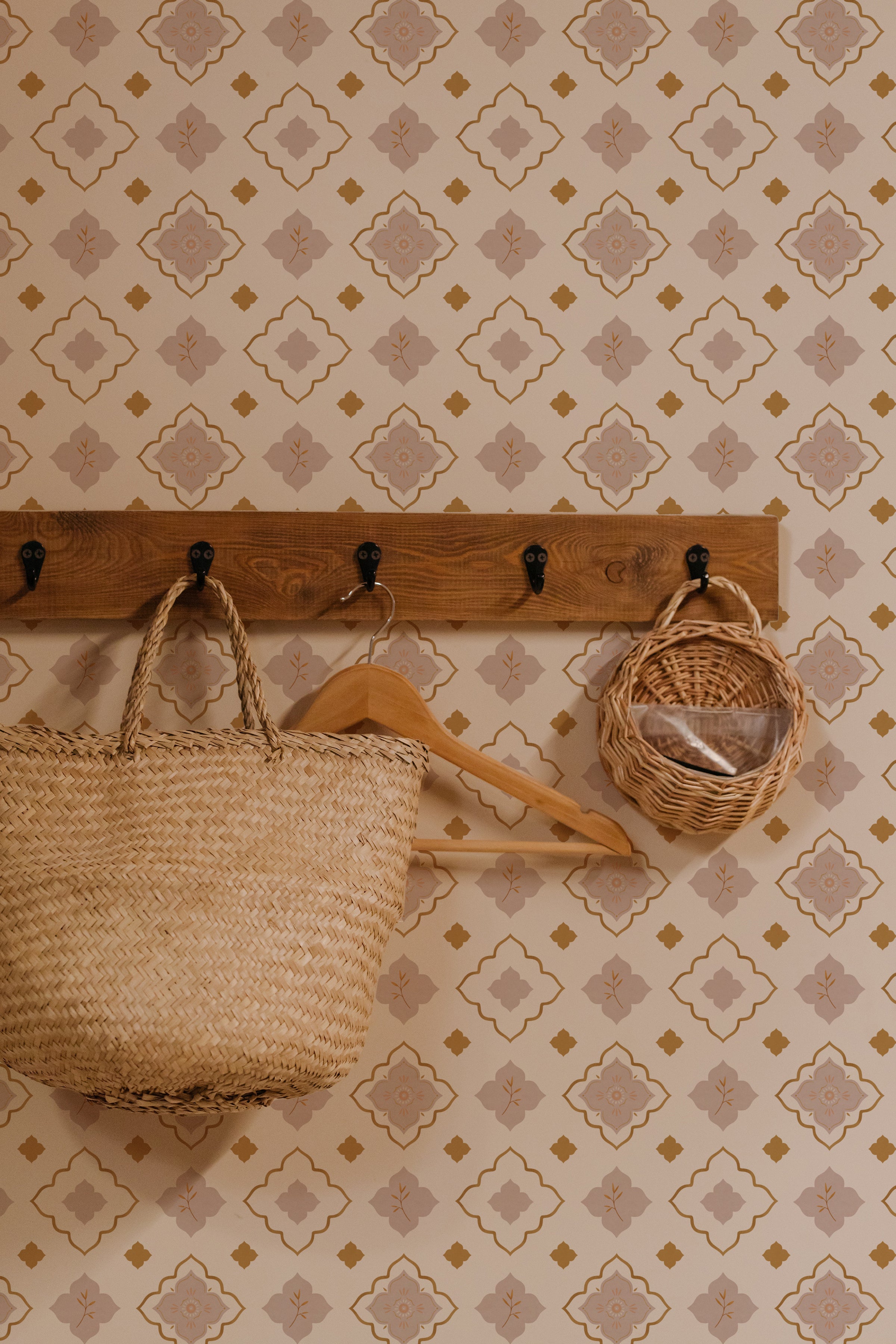 Wall-mounted wooden coat rack with hooks holding a woven tote bag and a small basket against a wall adorned with Moroccan Mosaic Wallpaper, featuring beige, blush, and gold geometric patterns