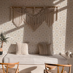 A cozy bedroom scene featuring a daybed with Moroccan Dream Wallpaper as the backdrop, adorned with a beige macrame wall hanging, set in a warmly lit room with wooden chairs and a plush rug