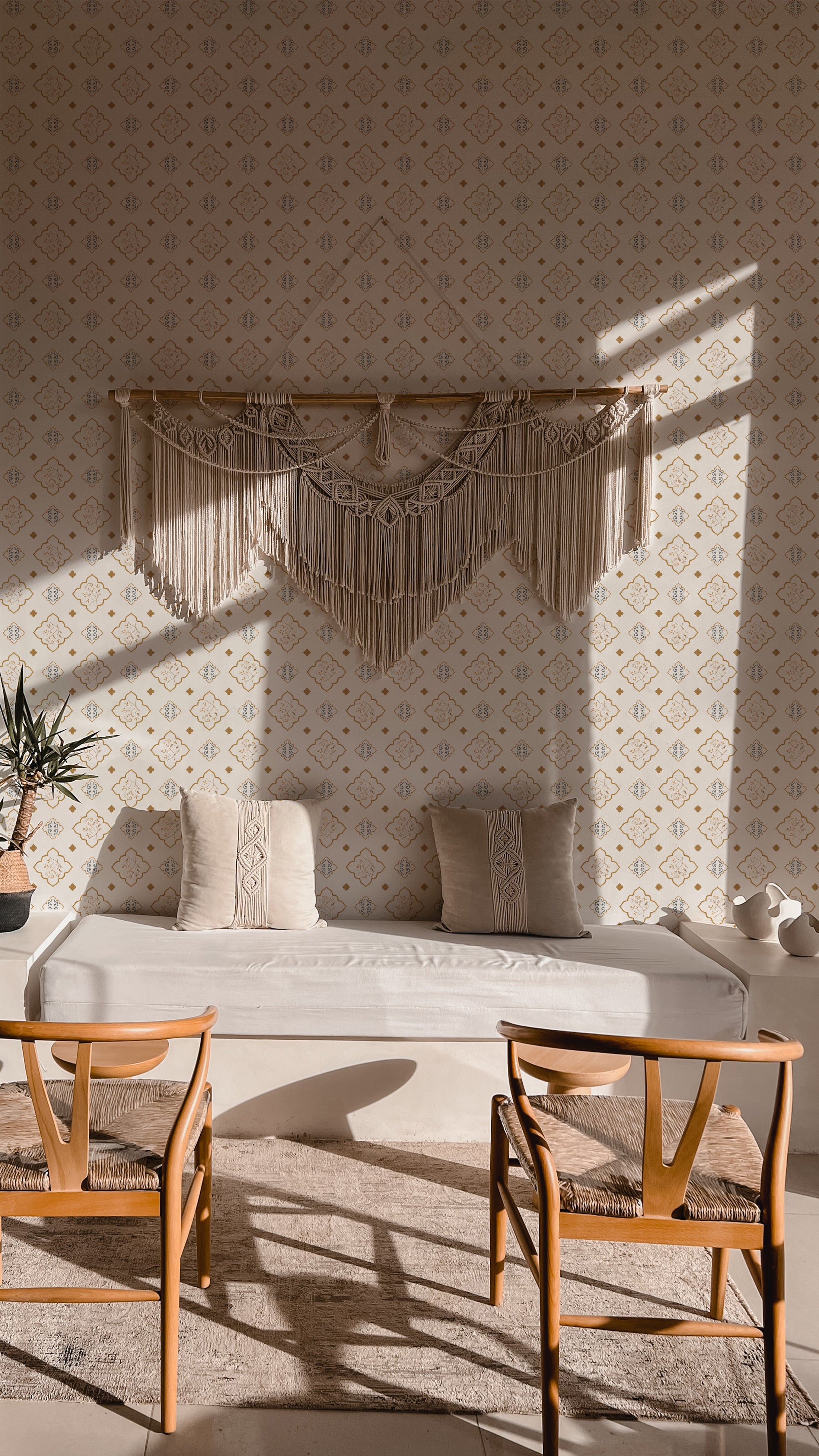 A cozy bedroom scene featuring a daybed with Moroccan Dream Wallpaper as the backdrop, adorned with a beige macrame wall hanging, set in a warmly lit room with wooden chairs and a plush rug
