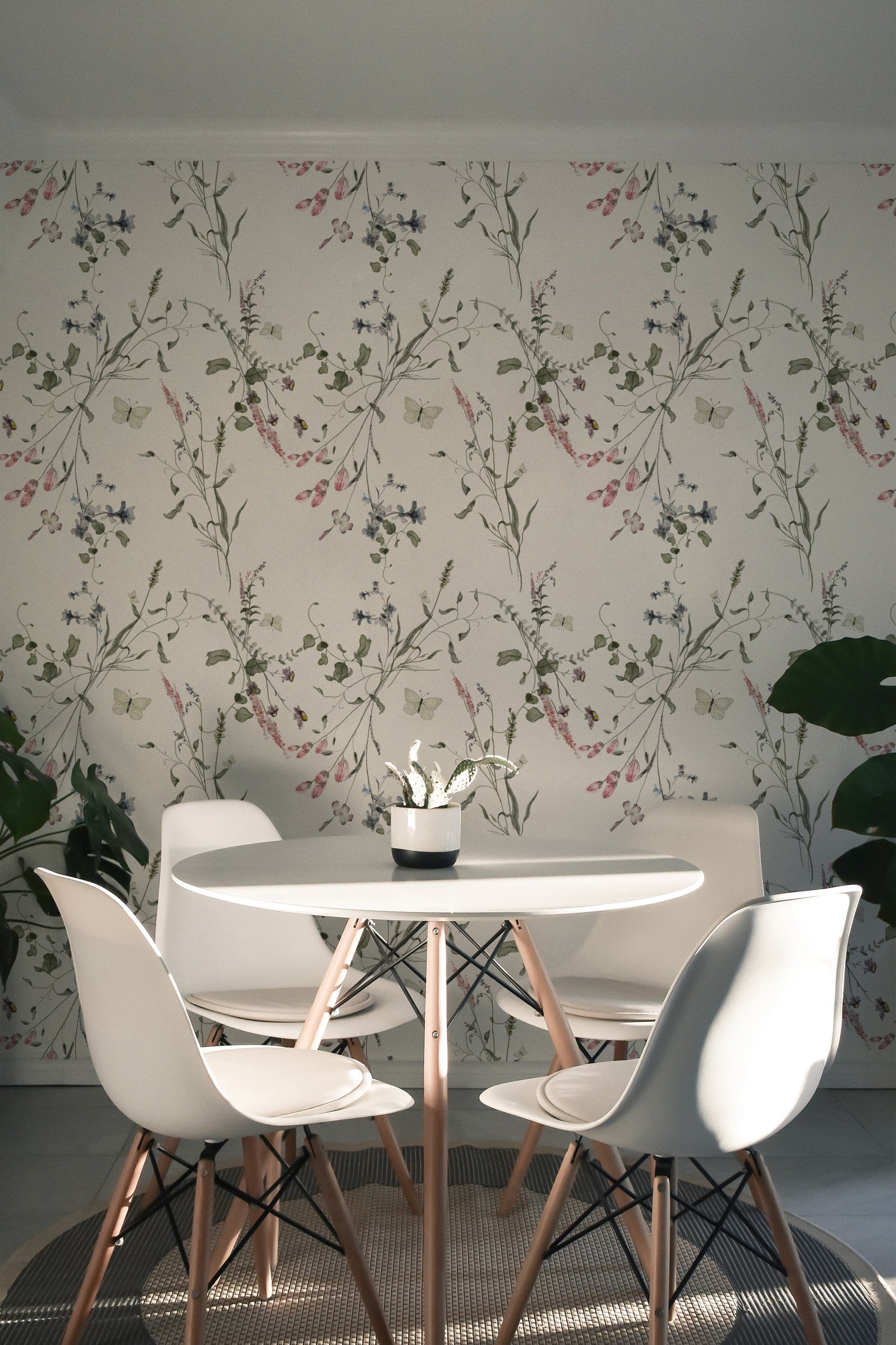 A modern dining area adorned with the Lovely Botanicals Wallpaper, which brings a fresh, natural vibe to the space. The light floral patterns provide a soft background for the sleek white table and chairs, enhancing the room’s contemporary aesthetic.