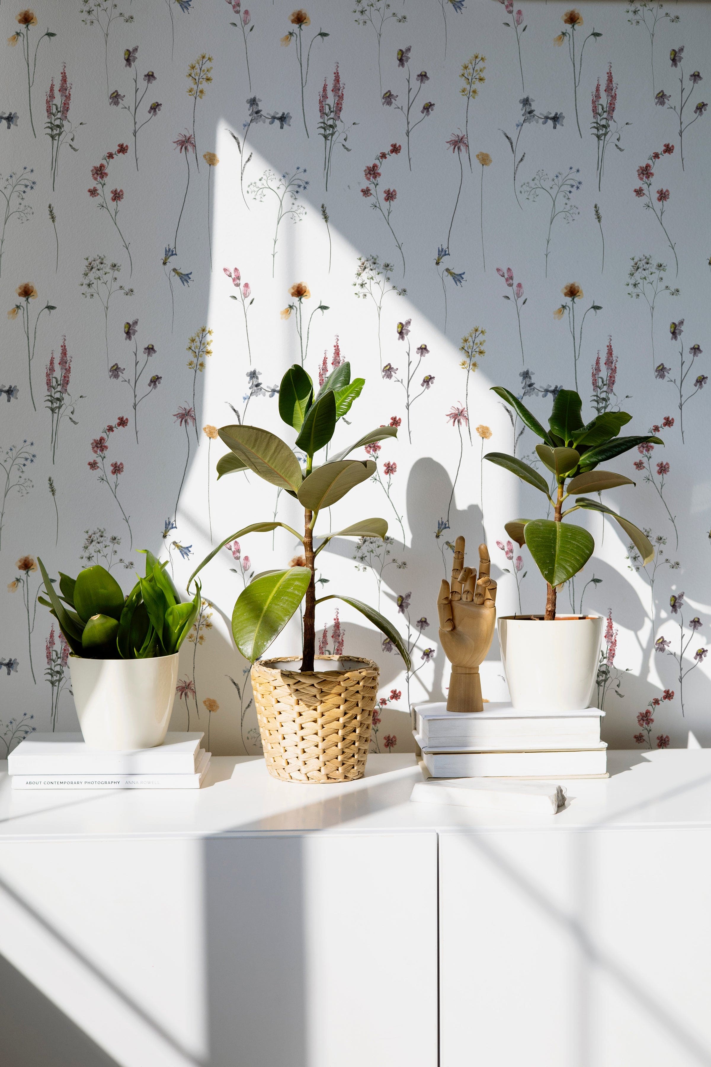 Bright, airy office space decorated with Dainty Botanicals wallpaper. Sunlight illuminates potted plants and books, highlighting the wallpaper's delicate botanical patterns.