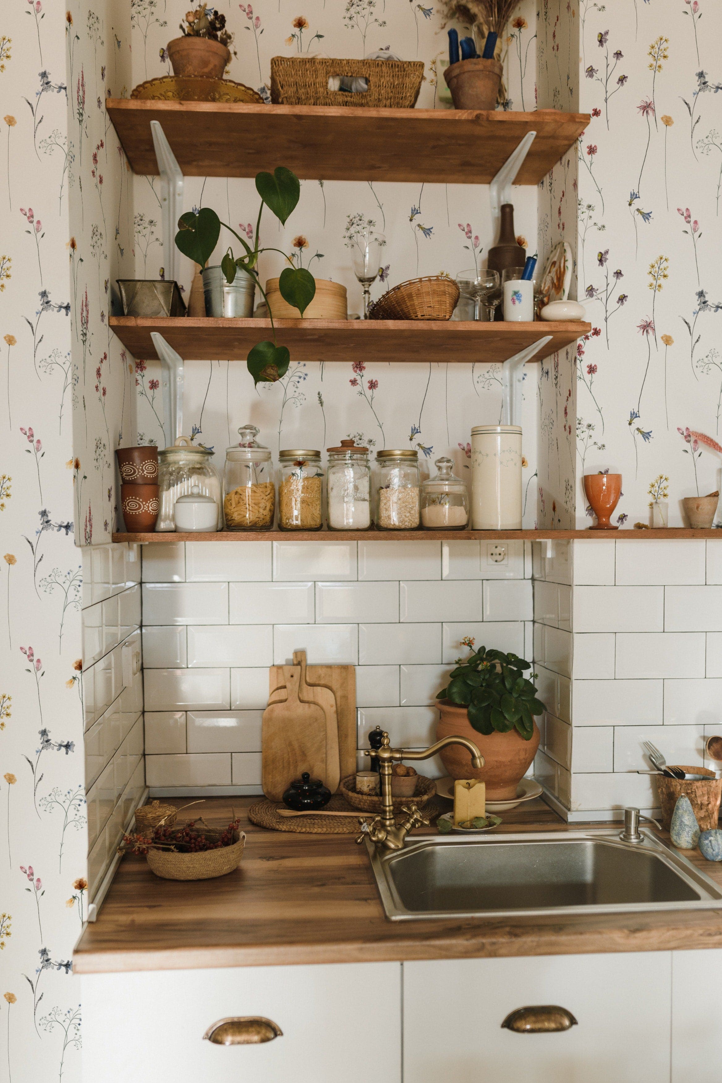 Rustic kitchen with Dainty Botanicals wallpaper enhancing a cozy corner filled with wooden shelves, assorted jars, and green houseplants against a backdrop of floral and botanical illustrations