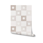 A roll of beige and white checkered wallpaper showcasing a regular pattern of white floral emblems set against beige squares. This wallpaper offers a neutral palette that adds warmth and elegance to any room, suitable for versatile interior styles.