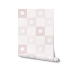 A roll of pink and white checkered wallpaper with a delicate white floral emblem pattern. The wallpaper exhibits a soft, textured look ideal for creating a warm, inviting environment.