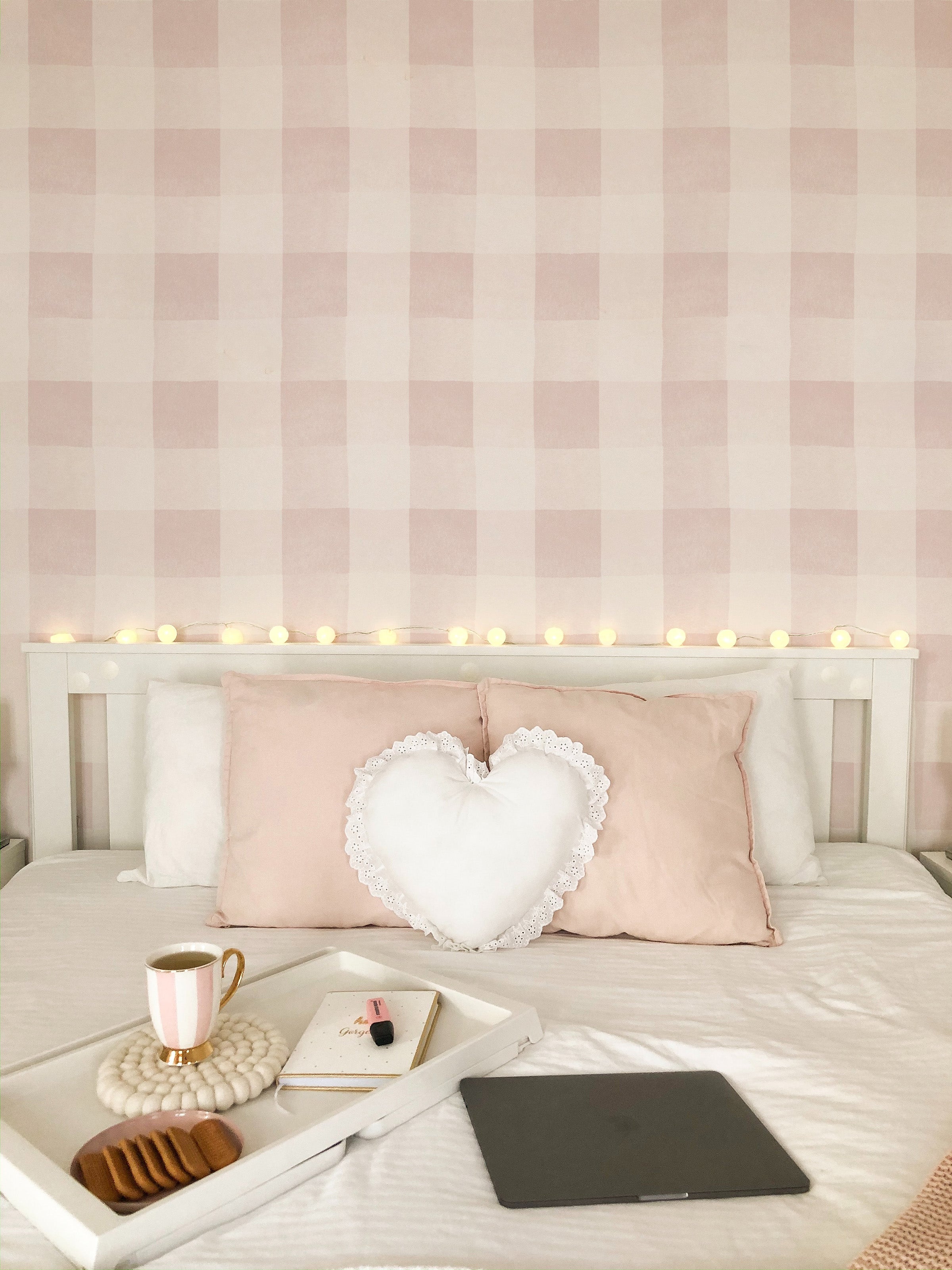 A cozy bedroom enhanced by Camille Wallpaper - Nude with its soft pink and white checkered design. The wallpaper adds a gentle, calming effect to the room, perfectly matching with the white and pink bedding and romantic decor accents, providing a tranquil retreat.