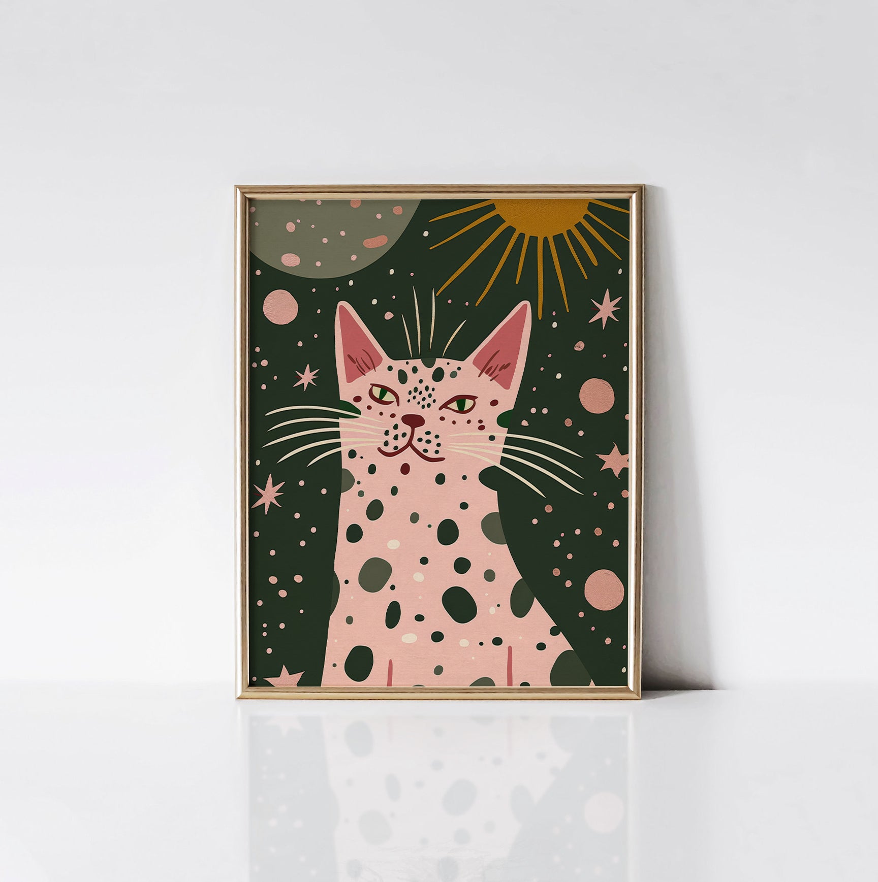 Galactic Cat Art Print framed in an elegant gold frame, showcasing a playful pink cat with green eyes and black spots surrounded by stars, planets, and a golden sun on a dark green background.