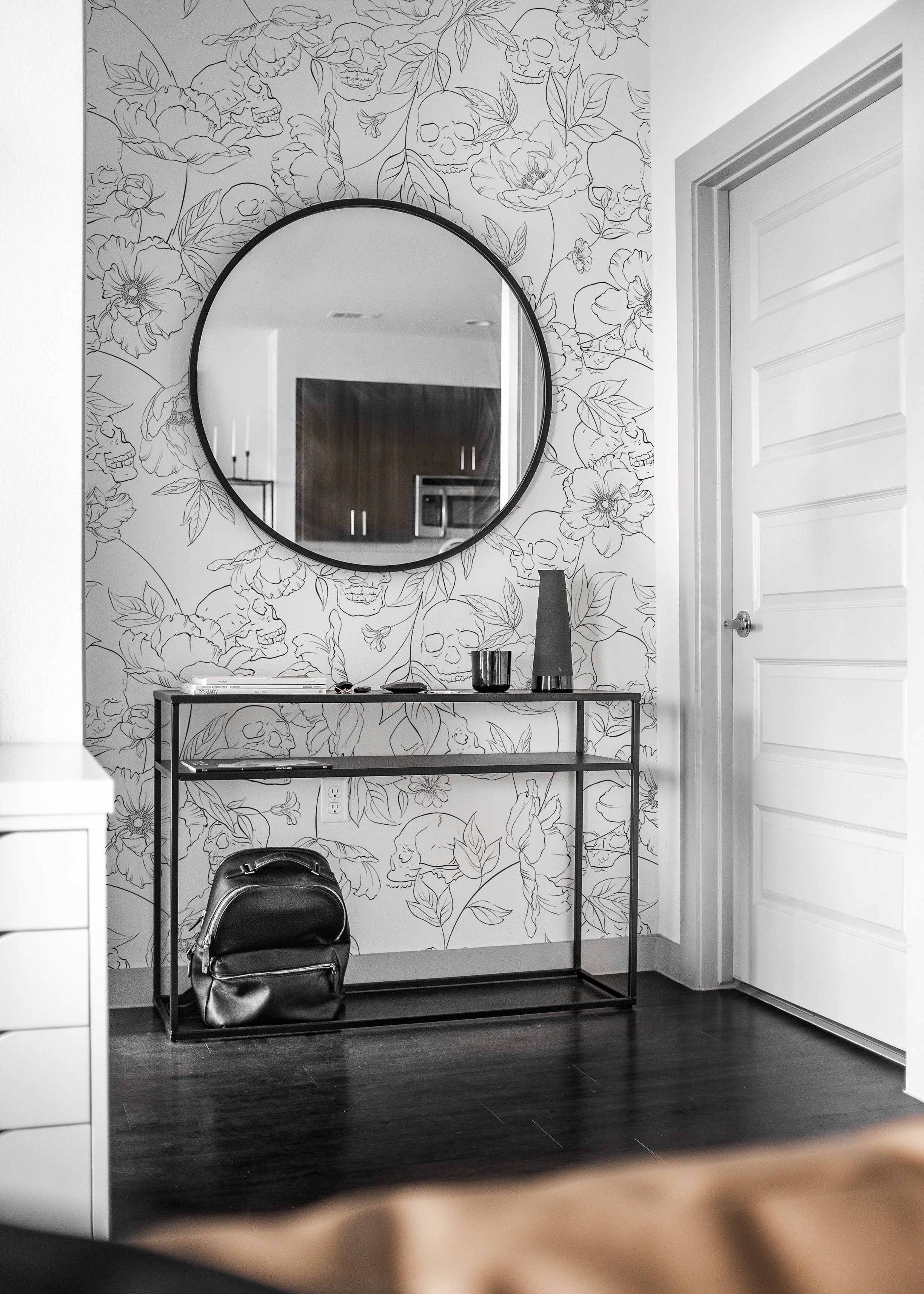 Elegant entryway decorated with Dainty Skull Floral Wallpaper, displaying a bold pattern of floral designs and hidden skulls in a line art style. A large round mirror and minimalist console table complement the wallpaper’s artistic flair.