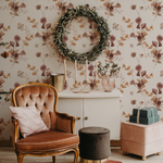 A charming corner decorated with Autumn Floral Wallpaper showcasing a vintage armchair and a holiday setup, including a festive wreath and elegant decor items, all complementing the rich floral patterns in rose and beige tones.