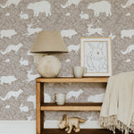 A rustic living space with a wooden shelf, ceramic lamp, and framed rabbit illustration against a beige wallpaper adorned with white woodland animals, including bears, foxes, and rabbits, providing a warm and inviting feel.
