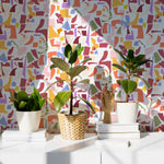 Modern living space featuring Geometric Jubilee Wallpaper with vibrant shapes and colors creating a playful and dynamic wall decor, complemented by minimalistic furniture and indoor plants