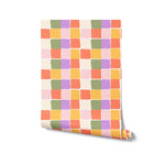 A rolled-up piece of wallpaper showing an abstract checker pattern with multiple colors including green, purple, orange, and pink. The colors are arranged in a cheerful and random order, giving the paper a lively and fun appearance.