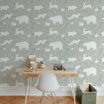 A home office with a light wooden desk and white chair placed against a green wallpaper adorned with white woodland animals including bears, foxes, and rabbits. The wallpaper provides a serene and natural backdrop.