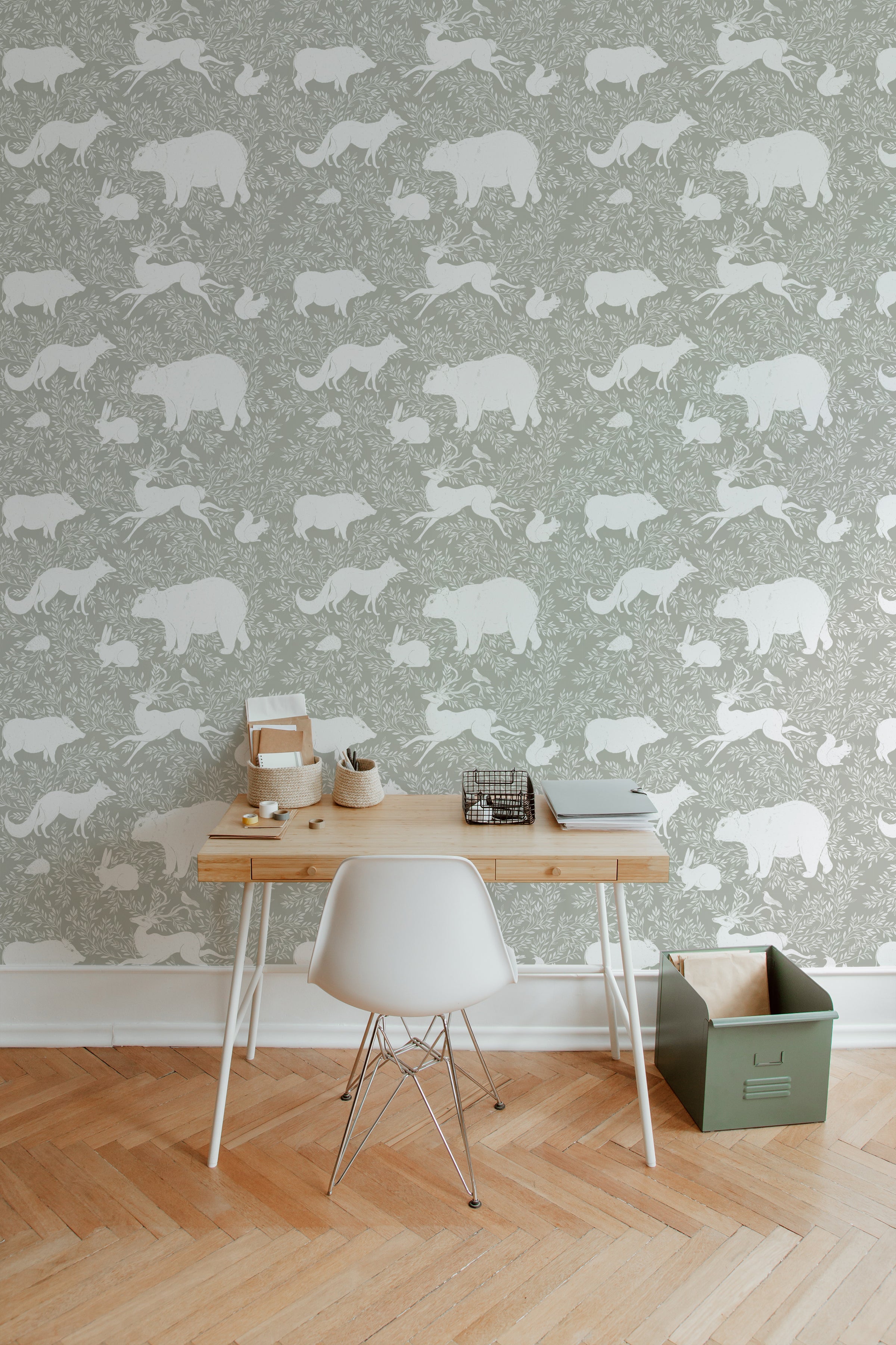 A home office with a light wooden desk and white chair placed against a green wallpaper adorned with white woodland animals including bears, foxes, and rabbits. The wallpaper provides a serene and natural backdrop.