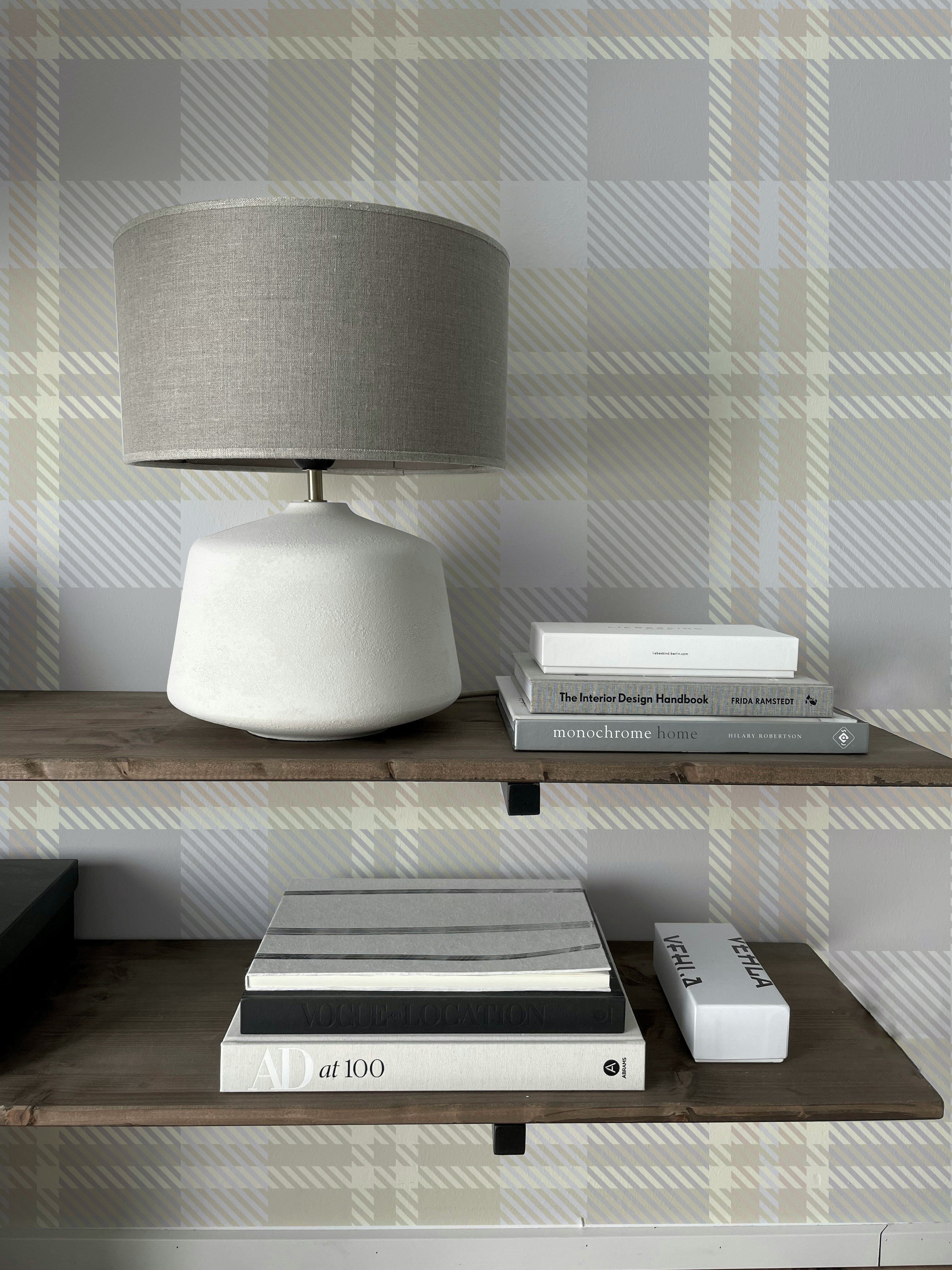 Close-up view of a shelf styled against Heirloom Tartan Plaid Wallpaper, displaying a lamp and books. The wallpaper's neutral tartan pattern adds a subtle yet elegant touch to the decor