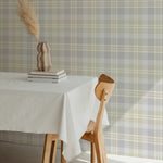 Interior view with Heirloom Tartan Plaid Wallpaper, showcasing a classic tartan pattern in neutral tones of gray, beige, and white. The wallpaper adds a cozy and traditional feel to the dining area, complemented by a simple wooden table and chair.
