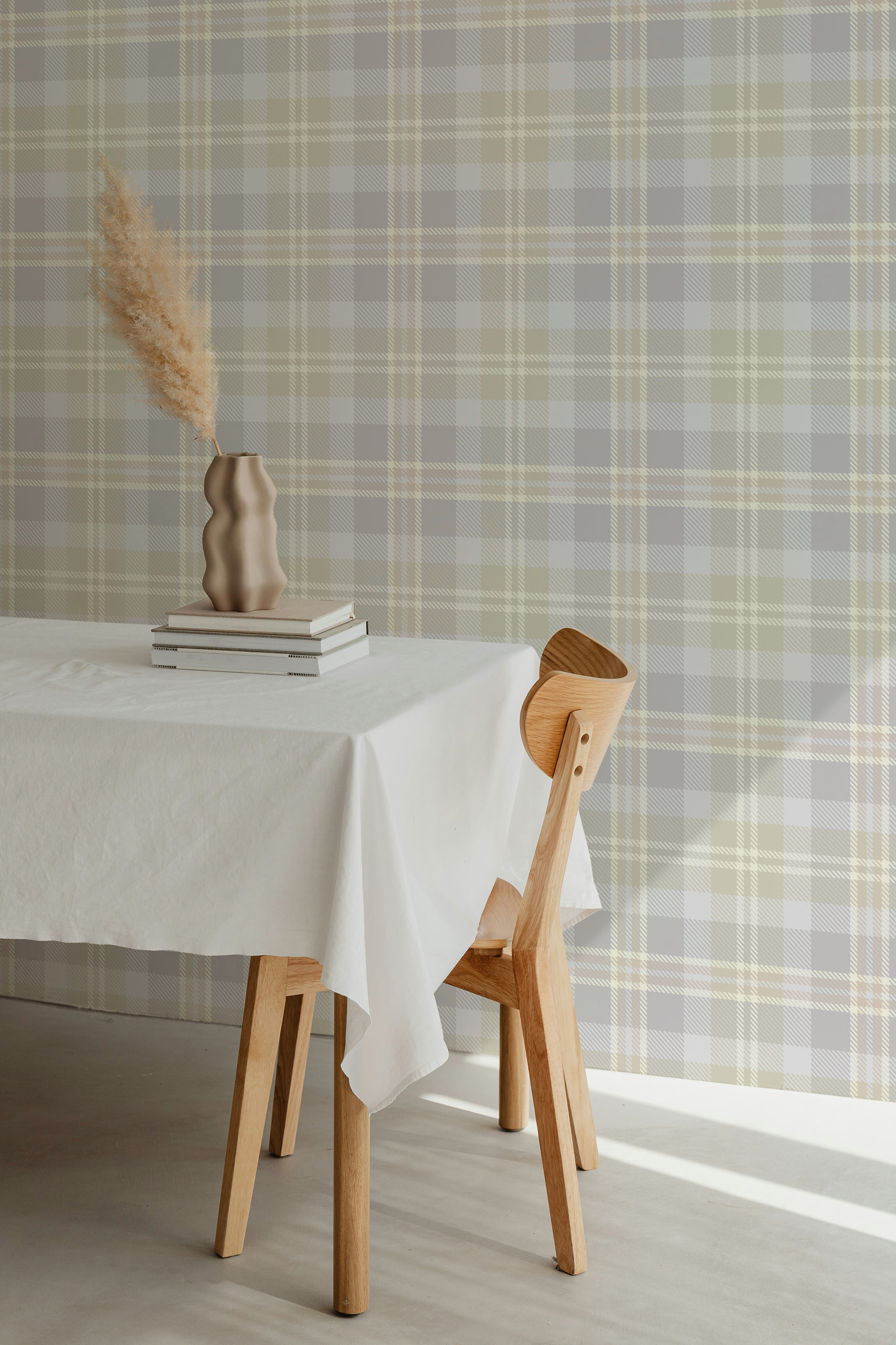 Interior view with Heirloom Tartan Plaid Wallpaper, showcasing a classic tartan pattern in neutral tones of gray, beige, and white. The wallpaper adds a cozy and traditional feel to the dining area, complemented by a simple wooden table and chair.
