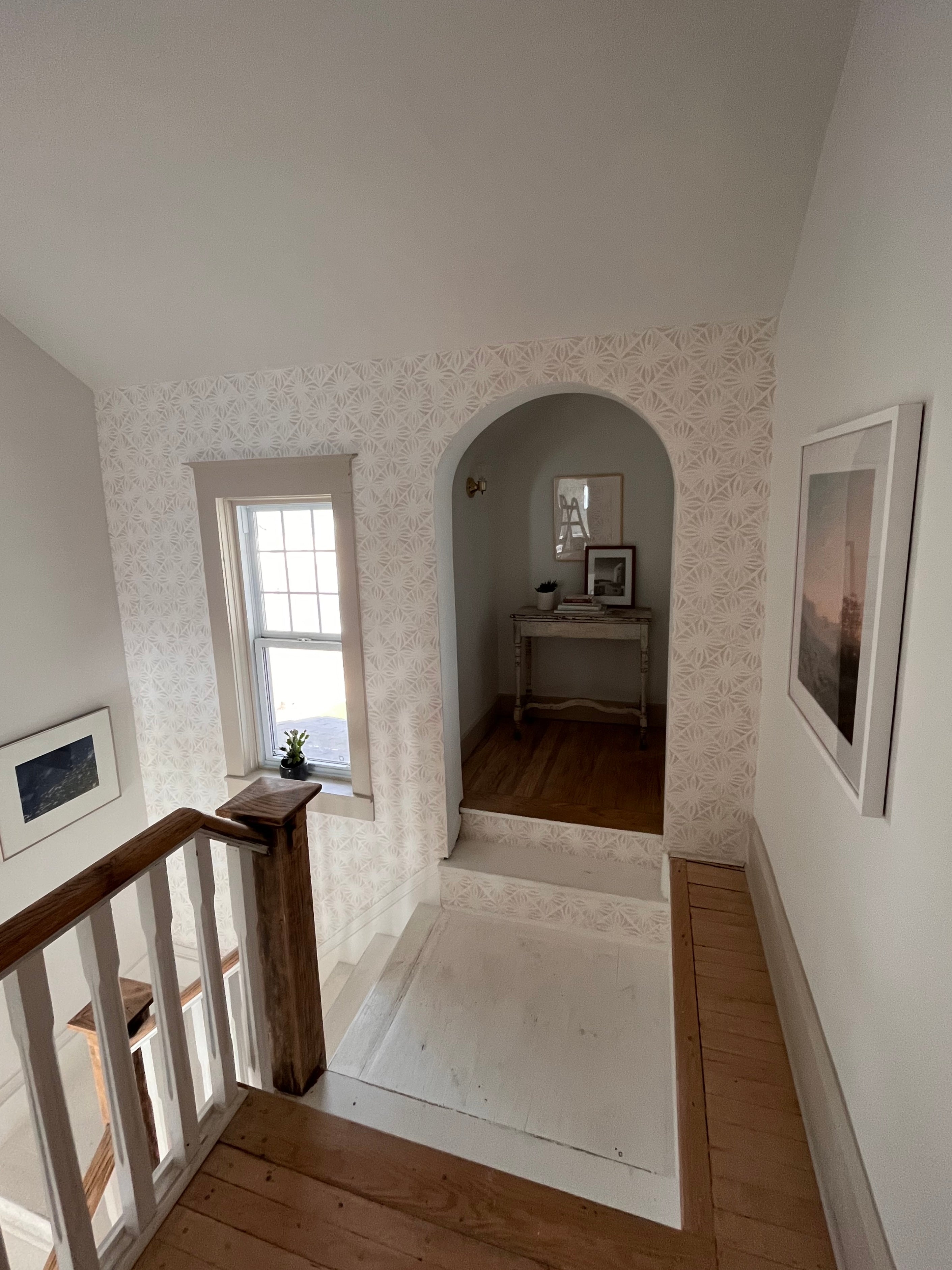 An inviting hallway featuring the Moroccan Tile Wallpaper II - Linen with a geometric pattern, creating a sophisticated visual texture. The scene includes a wooden staircase and a peek into a room with a classic white console table.