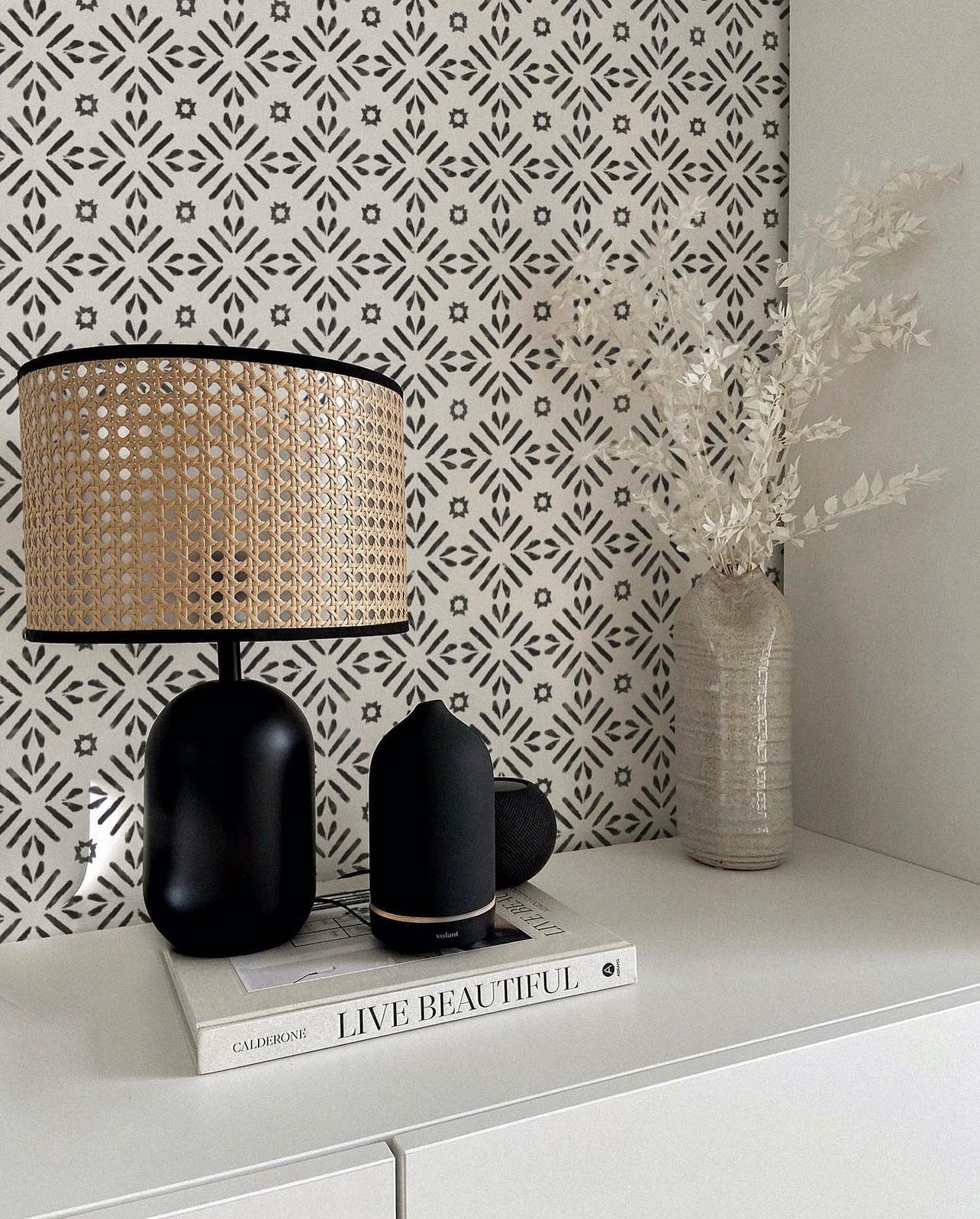 Modern workspace enhanced by Geometric Wallpaper III - Black, showcasing a detailed pattern of white geometric shapes on a black background, accompanied by a trendy lamp and decorative items on a sleek desk