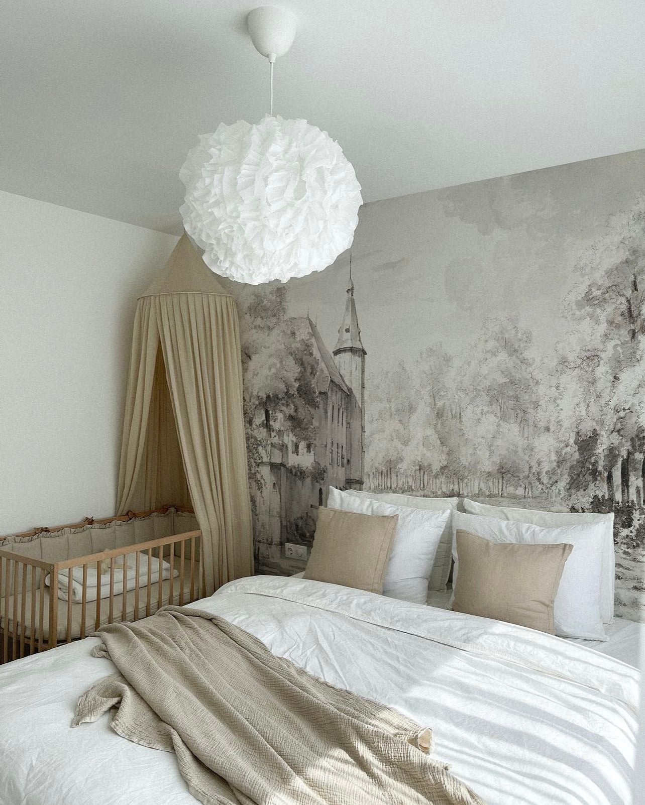 Charming nursery with a 'Kasteel Soelen - Wall Mural Wallpaper' showcasing a historic castle in a pastoral setting. The mural’s soft greyscale palette harmonizes with the room’s muted colors and plush bedding.