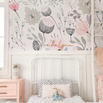 A cozy corner of a child's bedroom with the pastel floral wallpaper providing a delicate backdrop to a white metal bed adorned with a pink bedspread, a white and polka dot pillow, and soft toys, creating a dreamy and comforting atmosphere